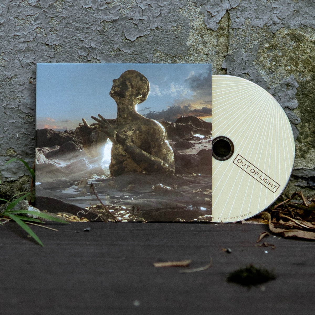 A CD and its case from Scary Kids Scaring Kids rest against a weathered wall. The Out of Light cover shows a statue-like figure rising with raised hands beneath a dramatic sky—a powerful image for this rock album.