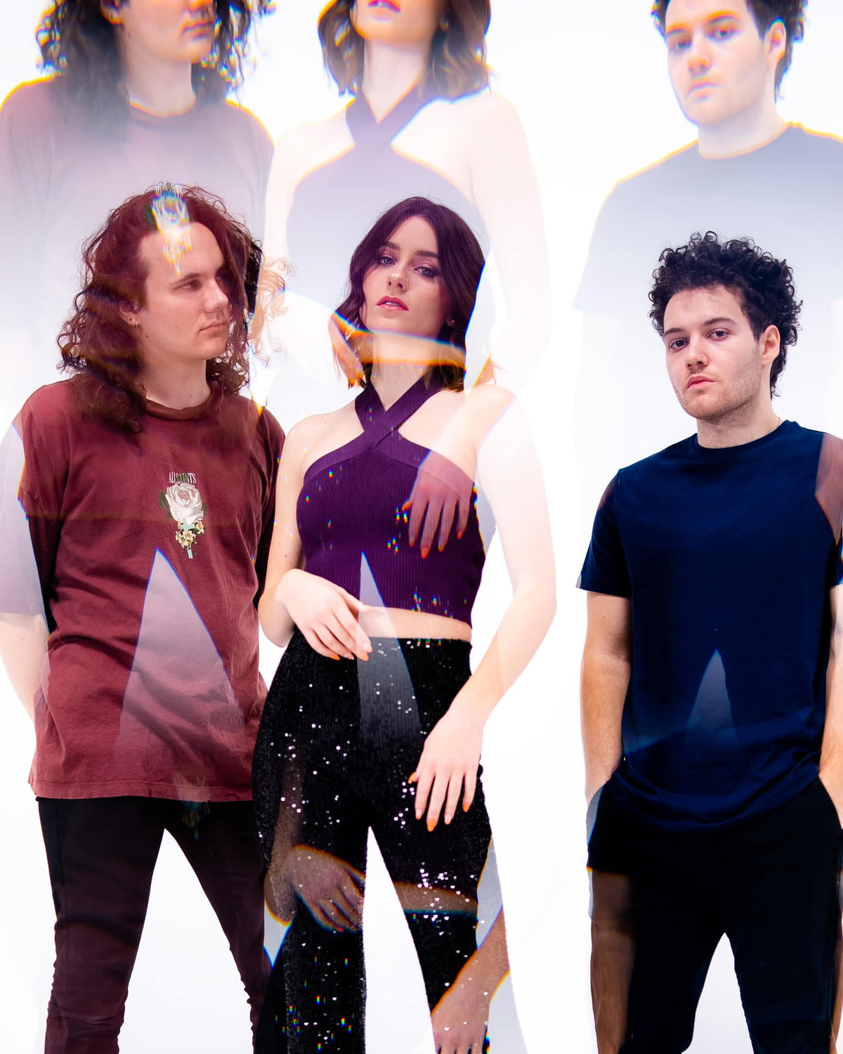 Three people stand against a white background, with colorful light reflections and ghostly duplicate images layered over them, creating a dreamy, surreal effect.