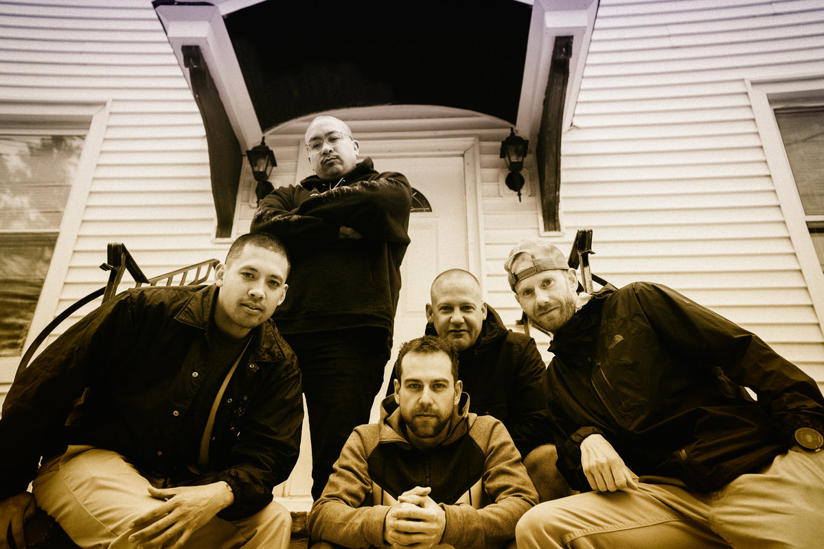 Five men pose on the steps of a white house, some standing and some sitting, all wearing jackets. The photo has a sepia tone, giving it a vintage feel.