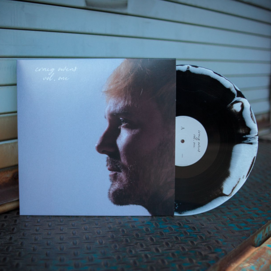 A limited edition Black & White splatter vinyl by Craig Owens is shown partly in its sleeve, which displays a profile photo of Craig Owens on a blue background. The cover reads Craig Owens vol. one—ideal for fans of Cemetery Weather.