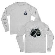 Image of the front and back of a white longsleeve. The left chest has a symbol that looks like two lines, with a circle in between them. the right sleeve says "jettison" in an outline black text. The back has a triangle outline with a circle outline around the triangle in black. there are dark grey/black rocks and a person standing on one of the rocks. around the circle in black texts "and so I watch you from afar".