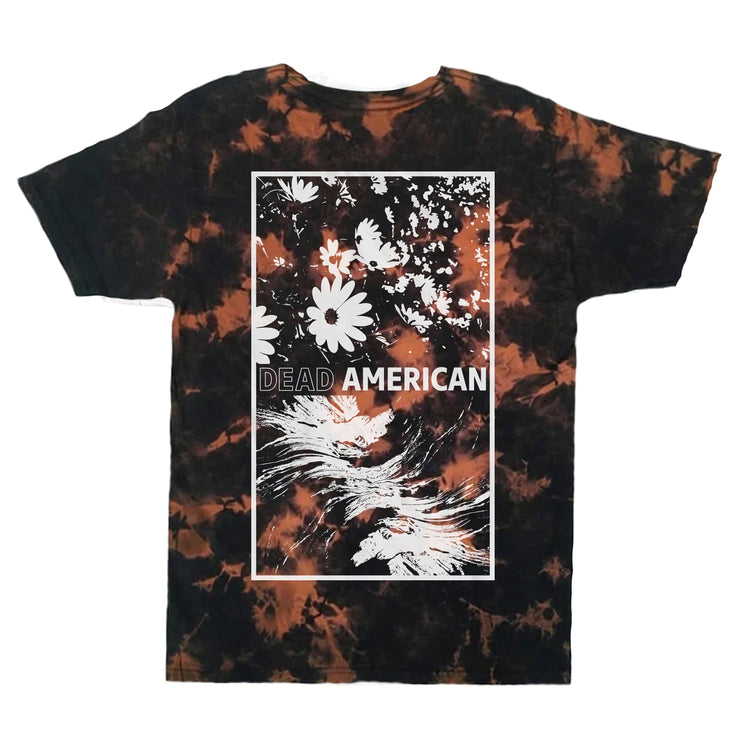 Image of a black tshirt with dark orange bleach color throughout the shirt. the center has a white outlined rectangle. inside the rectangle is a graphic of flowers floating around, below that in white reads "dead american". the word dead is written in a white outline, and the word american is written in a white outline with a white fill.