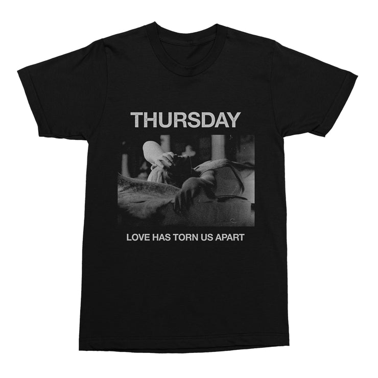 Black tshirt against white background. Across the chest in grey text reads thursday. below is a rectangle with a black and white photo of a person laying down with their hand covering their eyes. Below in grey is the text "love has torn us apart".