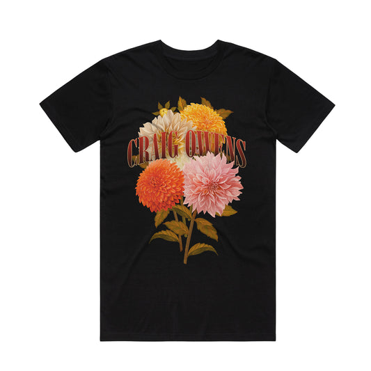 A black Craig Owens Flowers T-Shirt featuring a vintage-style illustration of four vibrant dahlias and green leaves, with CRAG QUEENS in bold lettering over the flowers.