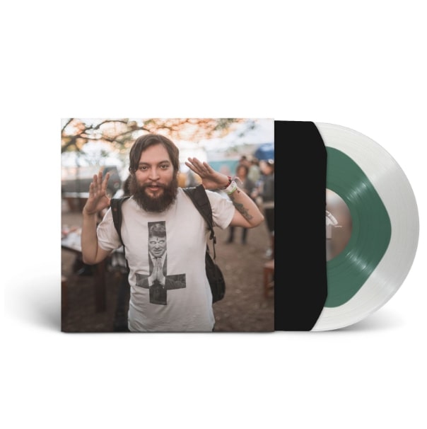 A limited edition mint green EVE 6 vinyl, partially out of its sleeve, shows a bearded man with a backpack raising his hands in a white graphic tee outdoors.