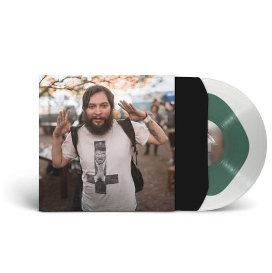 A limited edition mint green EVE 6 vinyl, partially out of its sleeve, shows a bearded man with a backpack raising his hands in a white graphic tee outdoors.