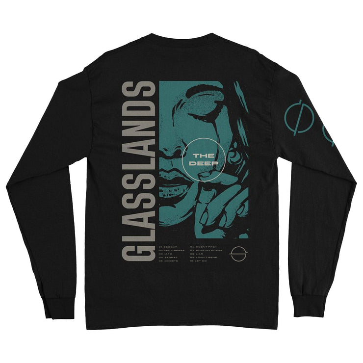 back of black longsleeve against white background. The right sleeve features a symbol of a circle with a horizontal line through the center multiple times descending down the sleeve in blue. The back says glasslands and there is a graphic of a woman's face up close crying and wiping a tear away. On top of this in a white circle reads "the deep". There is small white text below this, and another circle with a line through it symbol next to the small white text.