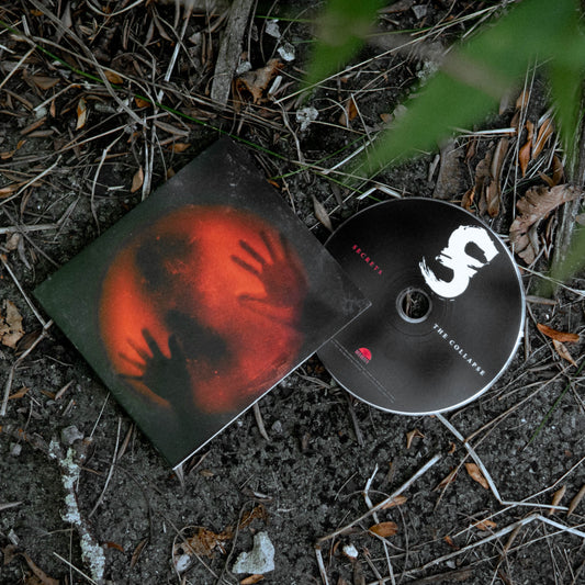A SECRETS CD titled "The Collective" and its case rest on the ground amid dirt and leaves. The case features hands reaching toward a red, glowing sphere; the CD has a large white S with minimal text—no tracklist or shipping date shown.