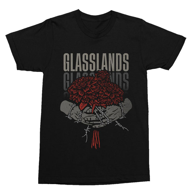 Black tshirt with light and dark grey text that reads "glasslands". Graphic of hands holding red flowers. The hands have white barbed wire wrapped around them.