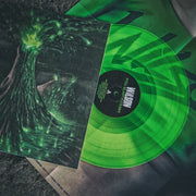 close up image of the wilson- full blast fuckery album artwork on a vinyl sleeve with the lime green vinyl sticking out of the sleeve. they are lying on a grey concrete background. the album cover features a green and dark red image of a volcano erupting with green light and lava. There are red and black clouds in the sky.
